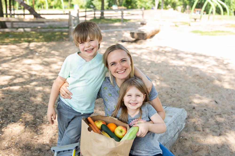 A woman and two children sitting outside with a bag of groceries
