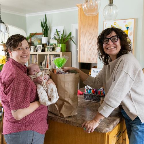 Adult couple standing in kitchen with infant and bag of groceries