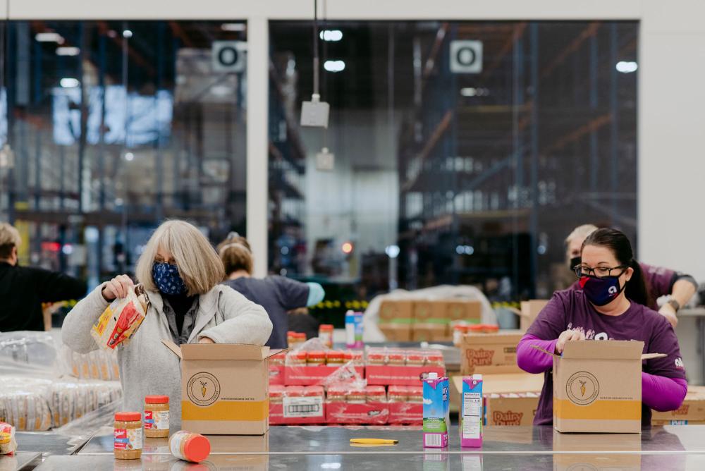 Two volunteers pack FOODRx boxes in an assembly line