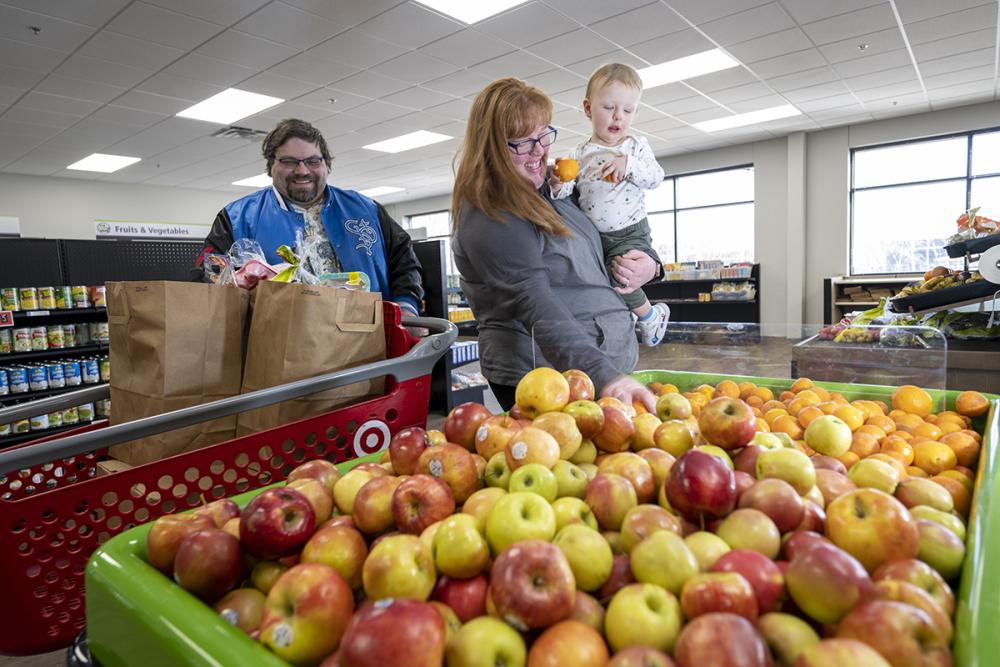 A mom and her child standing in front of apples at a food shelf