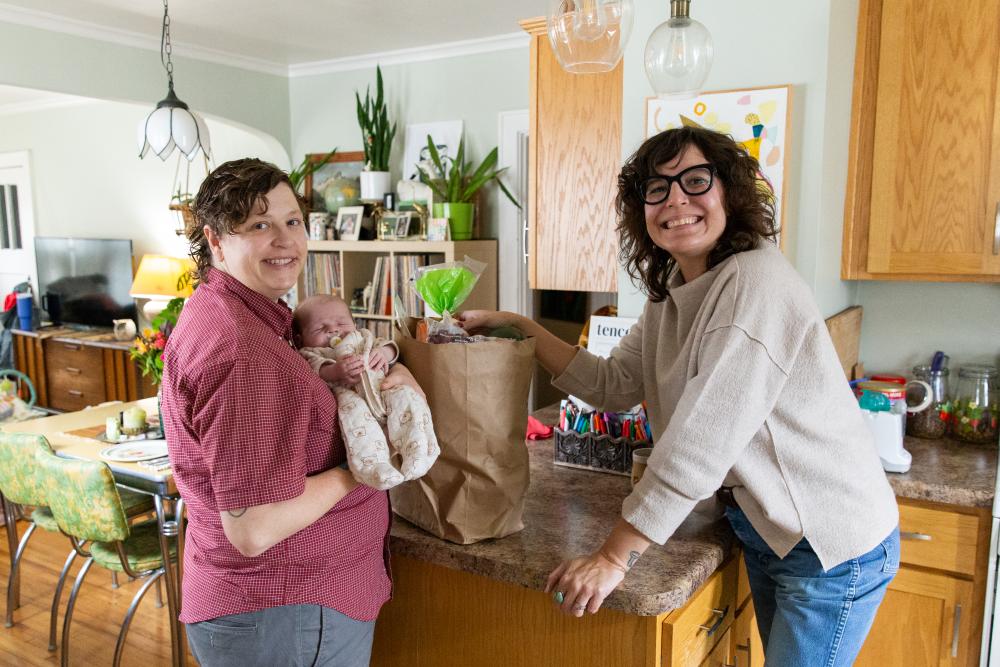 Adult couple standing in kitchen with infant and bag of groceries