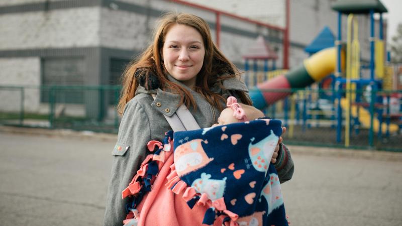 A woman with a baby smiles at the camera