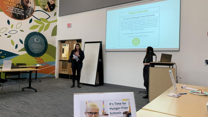 Rachel Sosnowchik and Maren Guptill from the Public Affairs Team present at the advocacy training session held at Second Harvest Heartland. The presentation shows a policy overview to “Invest in Hunger Free Schools.” A postcard on the table reads “It’s Time for Hunger-Free Schools.”