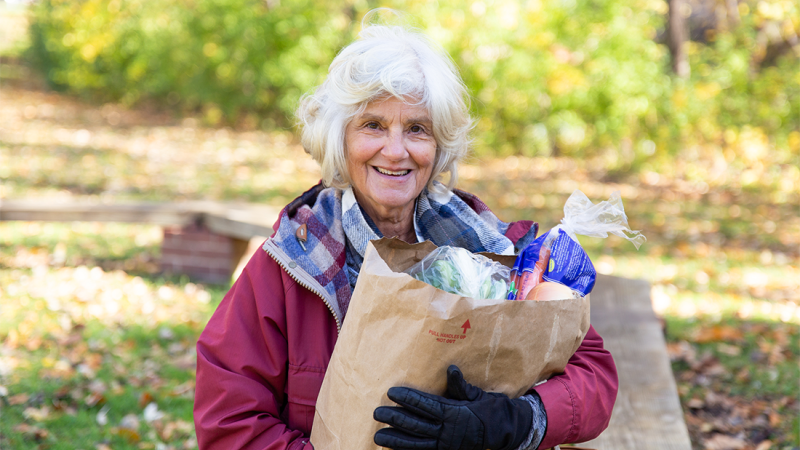 Woman smiling and standing with a grocery bag.