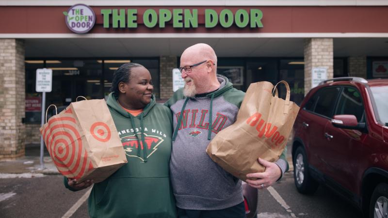 A couple looks at each other and smiles while holding bags of groceries