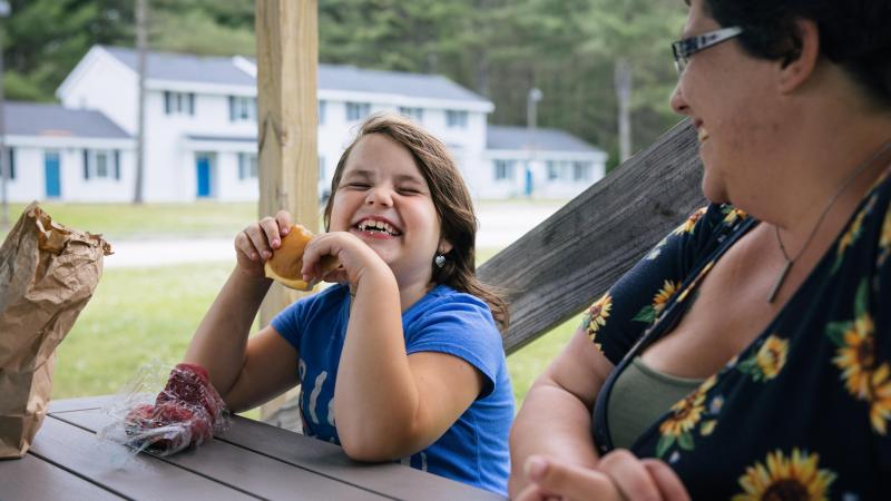 A girl eats food at a picnic table and laughs
