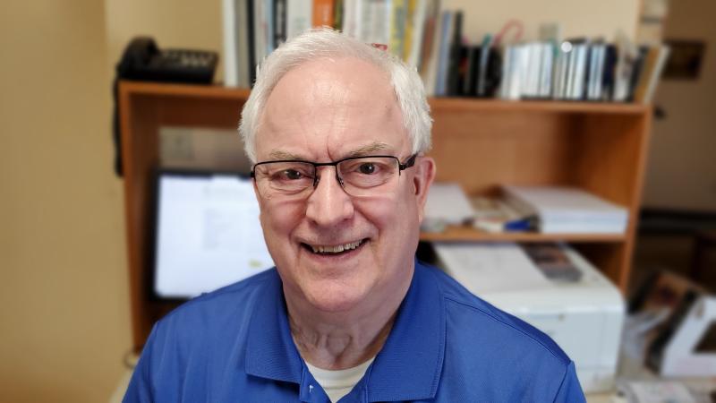 A older man smiles while sitting in office