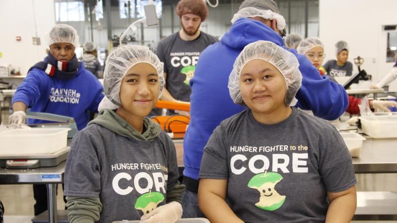 Two people smile at the camera while wearing hair nets in the Volunteer Center