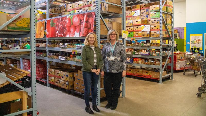 Two women stand in front of shelves of boxes