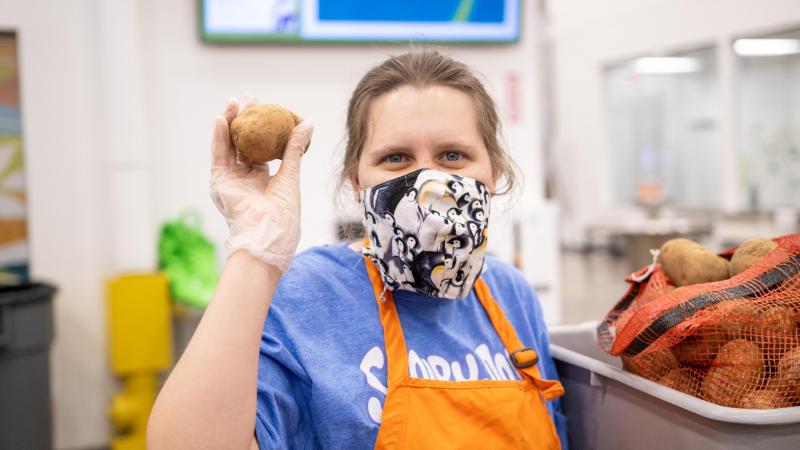 A volunteer holds a potato and smiles for the camera