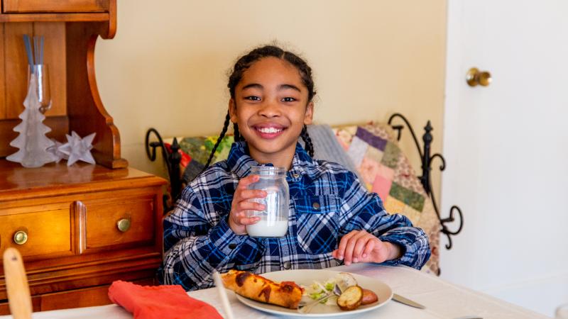 A young child at dinner table holding glass of milk