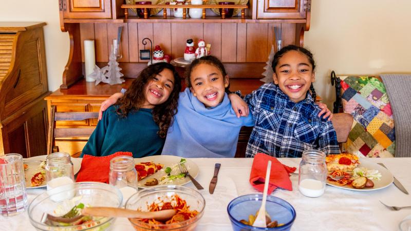 Three school-aged siblings smiling at a dining room table