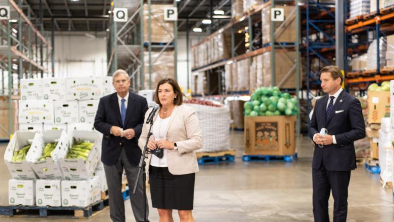 Leaders in agriculture and politics stand in a food bank warehouse speaking to media