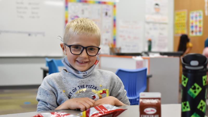 Boy with glasses eats lunch at school