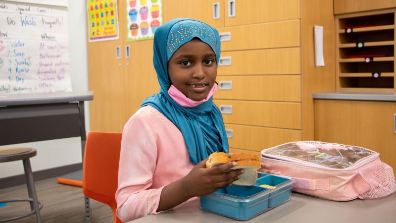 Young child in head scarf eating lunch at school