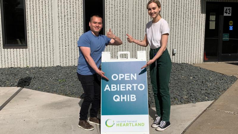 Two people stand beside an open sign with thumbs up
