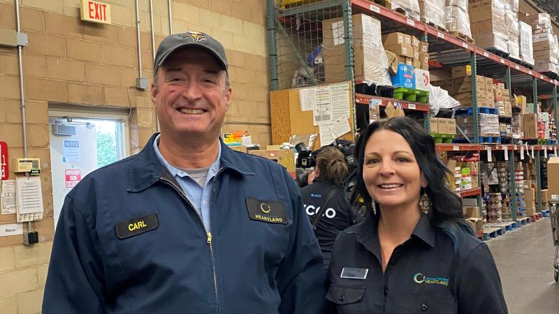 Two people smile standing in the loading doc of a grocery store