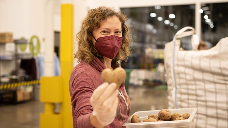 A volunteer holds out a heart-shaped potato during a food packing volunteer shift