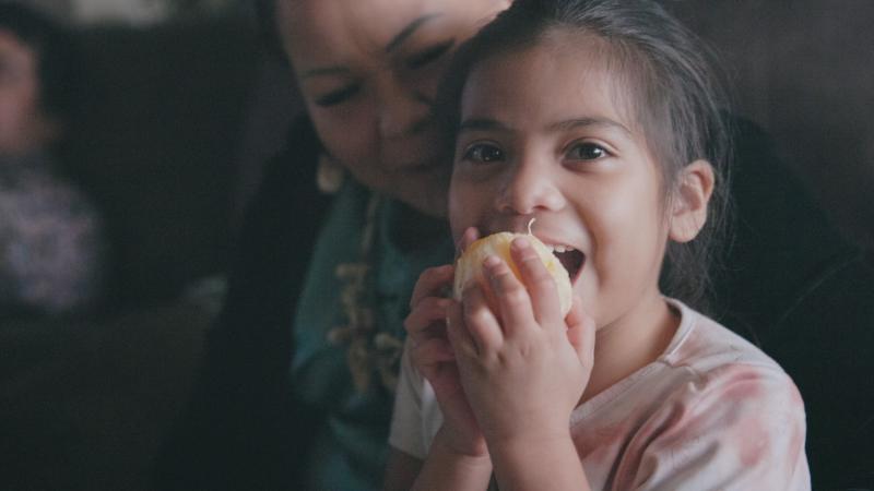 Child eats orange on lap of her mother