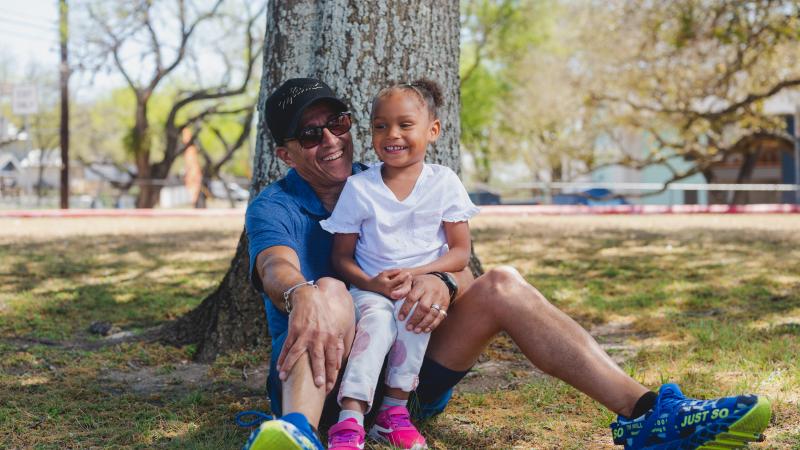 Dad sitting by tree with daughter in his lap, both smiling