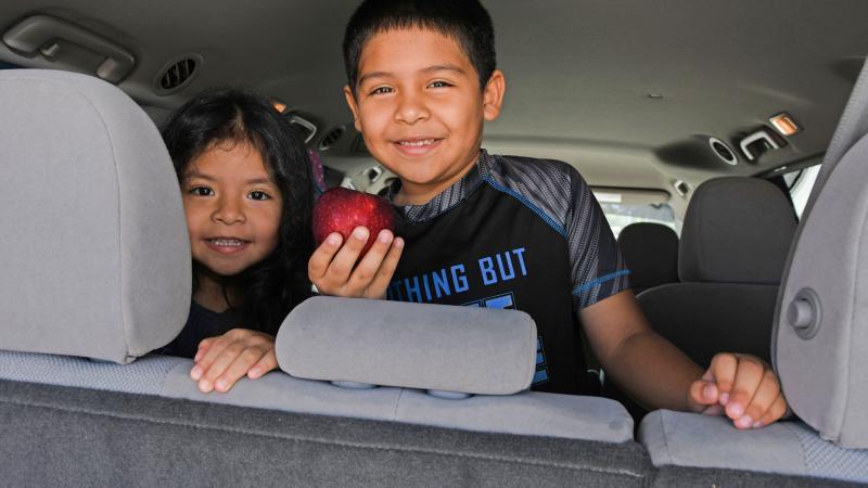 young girl and young boy smiling in a car, boy holding apple