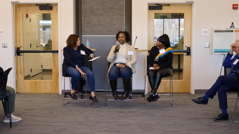 A woman speaks into a microphone as she sits on a panel of three speakers.
