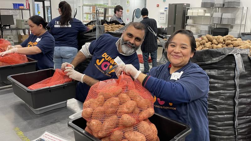 Two volunteers smiling at the camera while packing potatoes in the volunteer center.