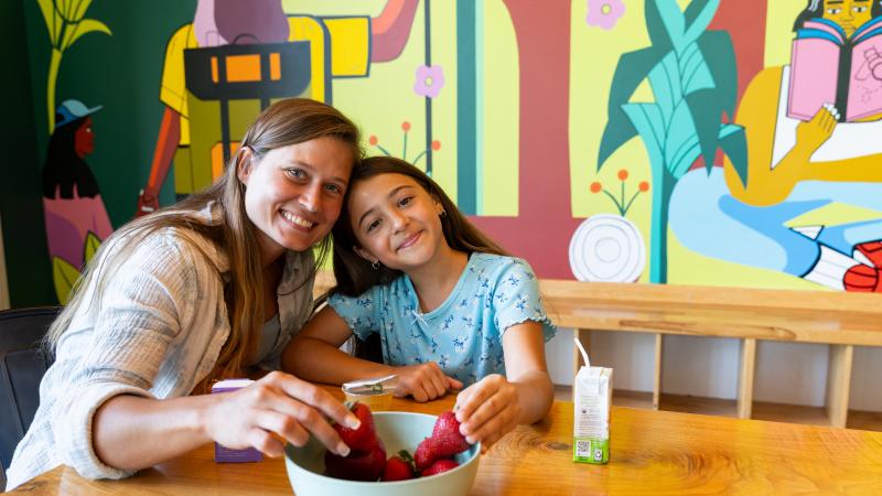 Adult woman with a child sitting at a table eating strawberries out of a bowl