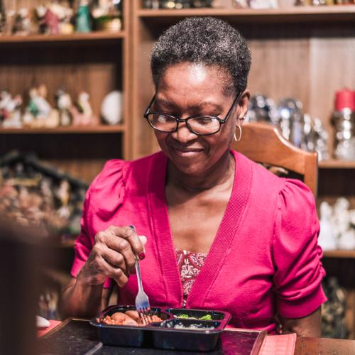 A senior woman eats a prepared meal in her home