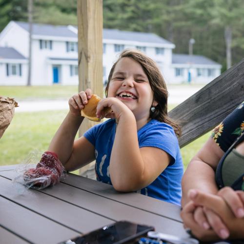 A girl eats food at a picnic table and laughs