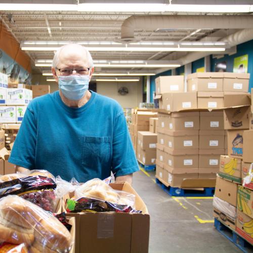 Man with face mask in front of boxes of food