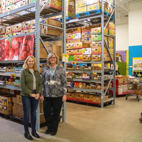 Two women stand in front of shelves of boxes