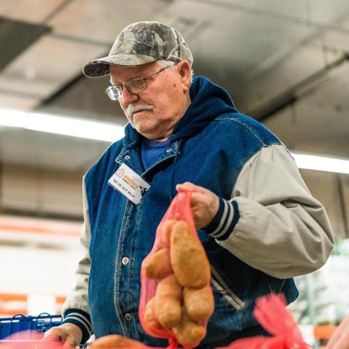 A senior man holds a bag of potatoes