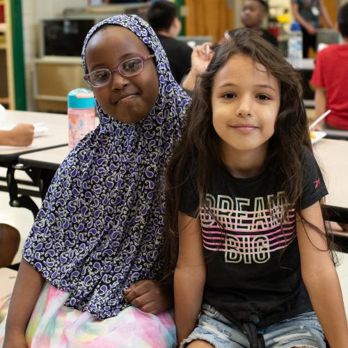 Two kids smile while sitting at lunchroom table