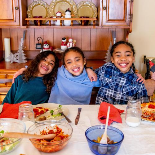 Three school-aged siblings smiling at a dining room table