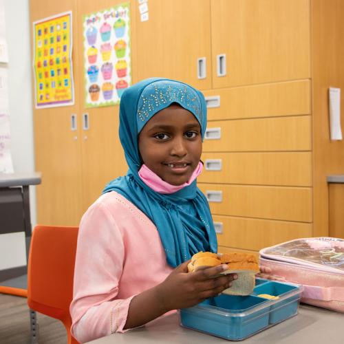 Young child in head scarf eating lunch at school