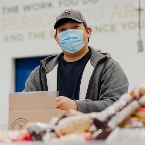 A volunteer smiles at the camera while packing a FOODRx box
