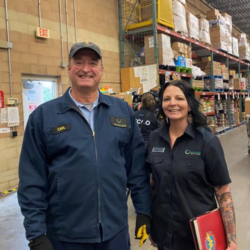 Two people smile standing in the loading doc of a grocery store