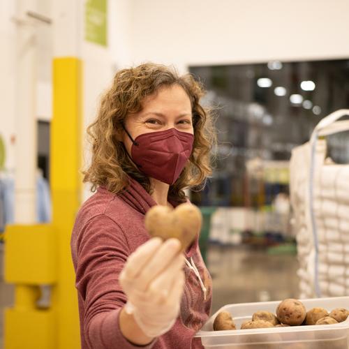 A volunteer holds out a heart-shaped potato during a food packing volunteer shift