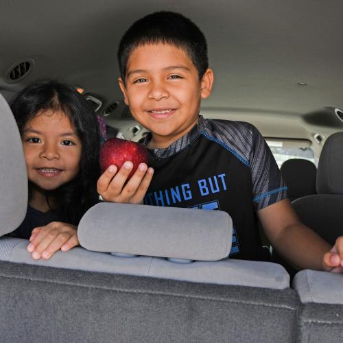 young girl and young boy smiling in a car, boy holding apple