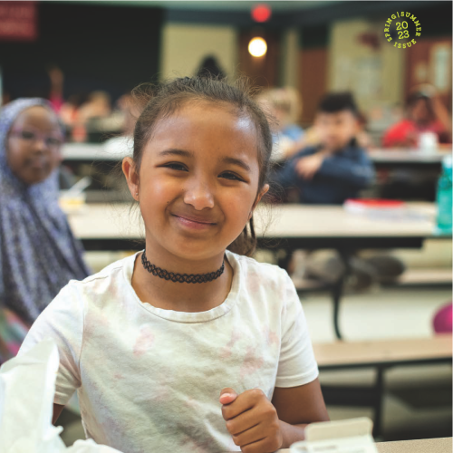 A child sitting at a lunch table with a tray of food in front of her