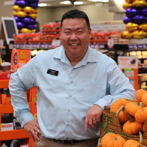 A grocer stands near a display of pumpkins
