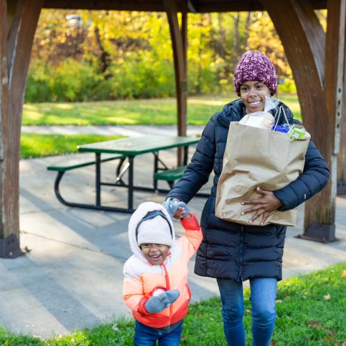 A mother and child walk through a park carrying groceries