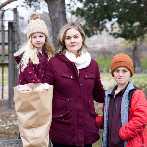 A woman and two children standing outside with a bag of groceries
