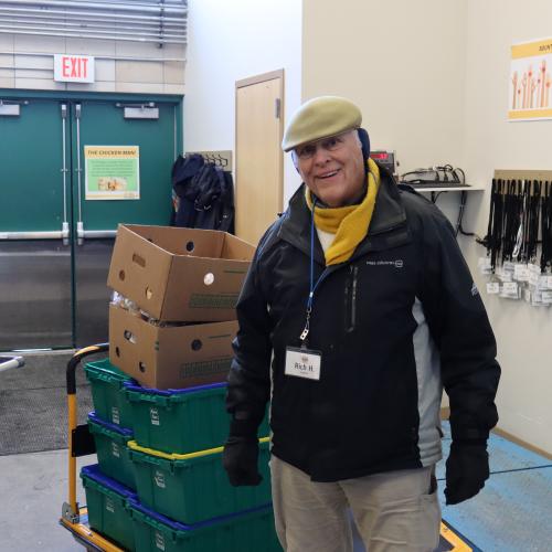 A man in a hat and coat standing next to a stack of bins