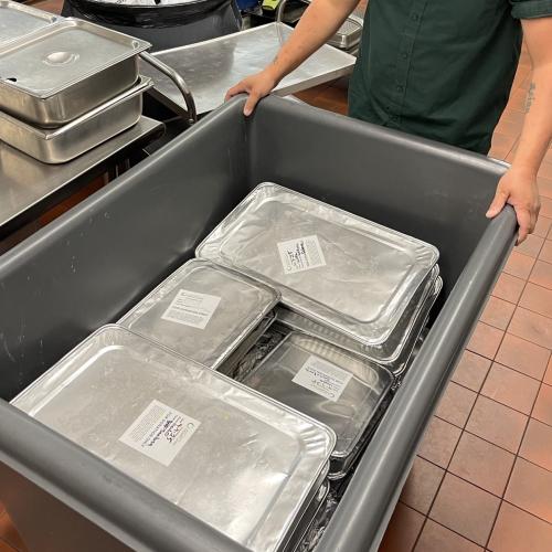 Person pushing cart of foil-covered pans of food