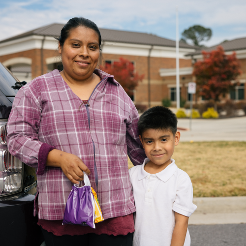 One adult holding a bag and one child standing in front of school -