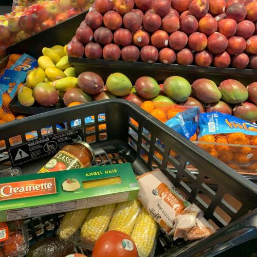 Cart in produce section of grocery store with pasta, sauce, produce and lentils in it