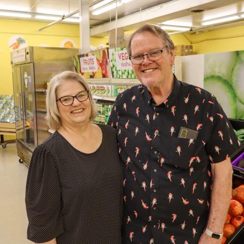 A man and woman posing in glasses and black shirts in a food shelf