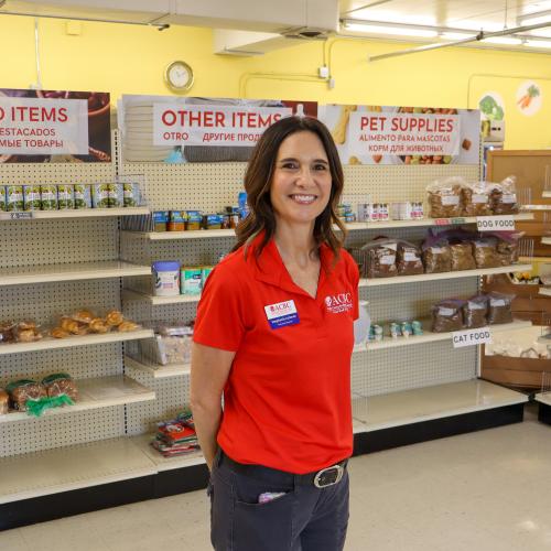 Stephanie Lehman, a brunette woman in a red shirt, stands in front of shelves of food